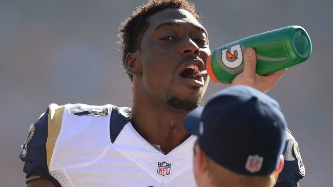 Football player drinks from a green bottle on the sideline